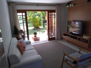 a living room with a white couch and a television at PRAIA DO FORTE - CONDOMINIO VILLAGE DAS ACACIAS - PISCINAS NATURAIS in Praia do Forte