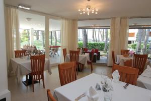 un ristorante con tavoli e sedie bianchi e finestre di Hotel Laura a Bibione