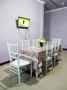 einen Tisch mit weißen Stühlen und einen TV an der Wand in der Unterkunft Kurnia Homestay in Ternate