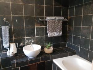 een zwart betegelde badkamer met een wastafel en een bad bij 440@Brooklyn in Pretoria