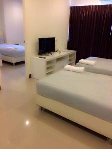 a bedroom with two beds and a desk with a television at BB Grand Residence in Pattaya