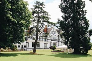 una gran casa blanca con árboles en el primer plano en The Manor at Bickley, en Bromley