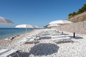 a row of white chairs and umbrellas on a beach at La Casa E Il Mare, Private Bay Hotel in Mattinata