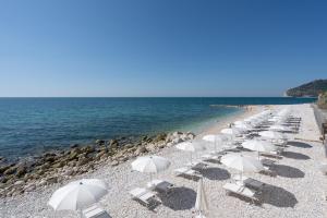 a row of white chairs and umbrellas on a beach at La Casa E Il Mare, Private Bay Hotel in Mattinata