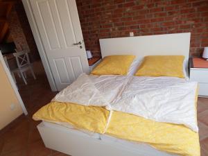 Cama blanca con sábanas amarillas y pared de ladrillo en Ostseeliebe-Oben-Rechts-1-KK-H en Hohwacht