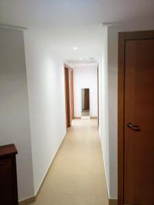 un largo pasillo con paredes blancas y una puerta de madera en Apartamento Angeles - Playa de Gandia, en Gandía