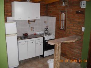 Una cocina con gabinetes blancos, estufa y refrigerador. en Cabaña Tío Miguel, en Los Molles