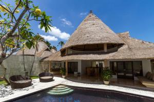 a house with a thatched roof and a swimming pool at Bvilla Seaside in Seminyak