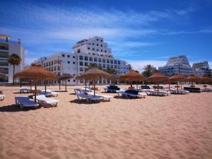 a sandy beach with chairs and umbrellas and buildings at Mare Viva Beach Apartment in Quarteira