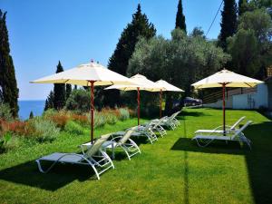 a group of chairs and umbrellas on the grass at Nikoli Apartments in Benitses
