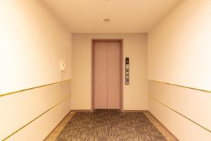 Sun Hotel Tosu Saga في توسو: ممر فاضي فيه باب وردي في غرفه فاضيه
