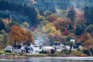 a village on the shore of a lake with autumn trees at Cairndow Stagecoach Inn in Cairndow