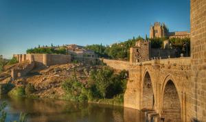 a bridge over a river with a castle in the background at Apartamento El Monasterio in Toledo