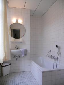 La salle de bains est pourvue de carrelage blanc, d'une baignoire et d'un lavabo. dans l'établissement Hotel Ten Putte, à Gistel