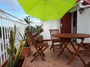 een tafel, stoelen en een groene parasol op een balkon bij TI-WAIT in Sainte-Anne