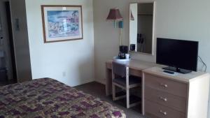 Habitación de hotel con escritorio, TV y cama en Heritage House Motel, en Prescott