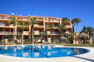 a swimming pool in front of a building with palm trees at Modern Ground Floor Calanova Golf Apartment in La Cala de Mijas