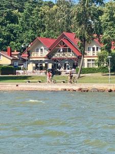 a building with people walking on the shore of the water at Kurenas in Juodkrantė