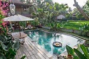 una piscina en un jardín con mesa y sombrilla en Gusde Tranquil Villas by EPS, en Ubud