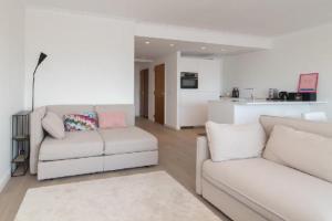 a living room with two white couches and a kitchen at sea and city view with double terrace Flat C Oostende in Ostend