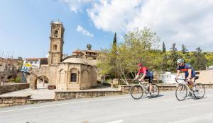 two people riding bikes down a street in front of a church at Cyprus Villages Hotel & Restaurant - Central Location - Bed & Breakfast - With Access To Pool And Stunning Views in Tochni