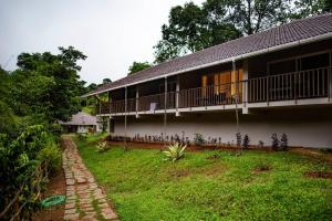a house with a balcony and a grass yard at Abad Brookside Wayanad in Vythiri