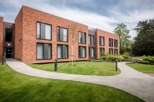un bâtiment en briques avec une cour herbeuse devant lui dans l'établissement Hinxton Hall Conference Centre, à Hinxton