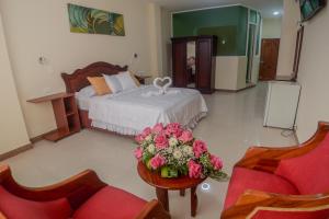 Victoria Suites Hotel في سانتو دومينغو دا لوس كولورادوس: غرفة نوم بسرير وطاولة عليها ورد