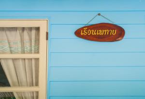 Un cartello appeso a un muro blu vicino a una porta di Tum Baan Suan ตุ่มบ้านสวน a Chanthaburi