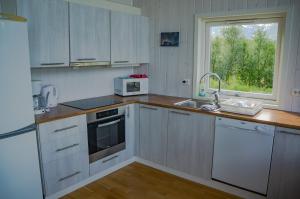 cocina con armarios blancos, fregadero y ventana en Aurora View Cabin en Lyngseidet