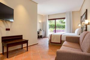 Habitación de hotel con cama, sofá y TV en Exe Layos Golf, en Layos