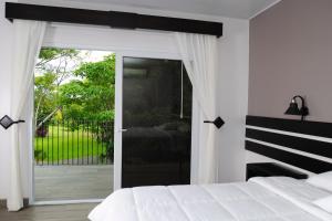 - une chambre avec un lit blanc et une porte coulissante en verre dans l'établissement Hotel Robledal, à Alajuela