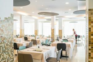een restaurant met witte tafels en stoelen en een vrouw die aan een tafel zit bij Hotel Parigi in Bibione