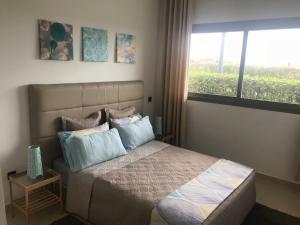 um quarto com uma cama com almofadas e uma janela em Appartement Blanca Beach em Sidi Rahal
