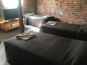 a room with two beds and a tv and a brick wall at Centennial Hotel Gulgong in Gulgong