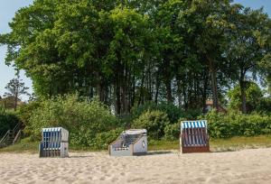 3 chaises assises sur le sable sur une plage dans l'établissement Schlafstrandkorb Nr.2, à Sierksdorf