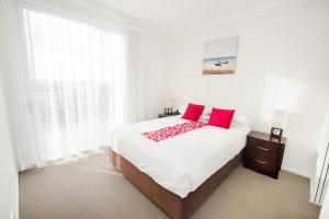 a white bedroom with a large bed with red pillows at Curtis Central Apartments in Gladstone