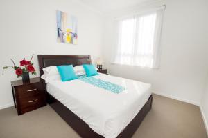 a bedroom with a bed with white sheets and blue pillows at Curtis Central Apartments Official in Gladstone