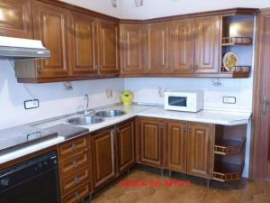 cocina con armarios de madera, fregadero y microondas en Casa del Sol en Zahara de los Atunes