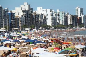 a crowd of people on a beach with umbrellas at Edf Gil Nogueira-Praia Morro-Guarapari-3º Andar-APTO FTE-SOL MANHA-Piscina-Sauna-02 quartos com Ar -TV Tela Plana-Wi-Fi-Varanda Gourmet -Tela de Proteção - Purificador Água-Airfray-Dois elevadores-01 Garagem-Portaria 24 horas-50 mts da Praia do Morro in Guarapari