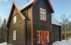 a black cabin with a red door in the snow at Cozy Home In Engerdal With House A Mountain View in Femundsundet