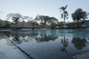 an empty swimming pool with palm trees and buildings at Alit Beach Resort and Villas in Sanur