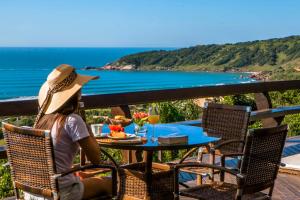 a woman sitting at a table with a view of the ocean at Solar Mirador Exclusive Resort e SPA in Praia do Rosa