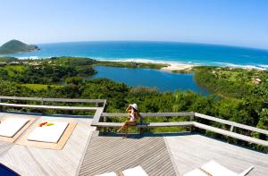 a woman is sitting on a balcony looking at the ocean at Solar Mirador Exclusive Resort e SPA in Praia do Rosa