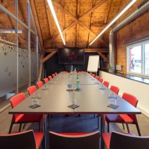 une grande salle de conférence avec une grande table et des chaises rouges dans l'établissement Le Manoir Vionnaz, à Vionnaz
