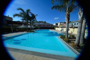 a large blue swimming pool with palm trees and buildings at Case Vacanze Ancora in Porto Empedocle