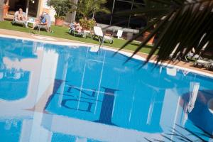 una gran piscina azul con gente sentada en sillas en Hotel Duque de Najera, en Rota