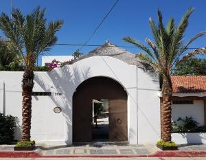 a white building with a door and two palm trees at Los Milagros Hotel in Cabo San Lucas