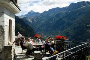 un grupo de personas sentadas en una mesa en un balcón con montañas en Hotel Roseg, en Chiesa in Valmalenco