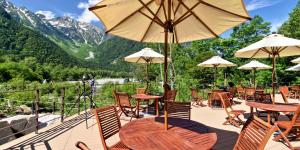 un patio con mesas y sillas con montañas en el fondo en Kamikochi Hotel Shirakabaso en Matsumoto